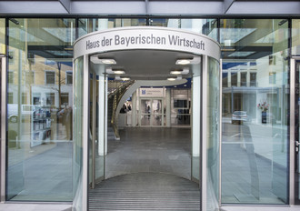 Foto vom Eingang in Haus der Bayerischen Wirtschaft und Blick in die ConferenceArea des ConferenceCenters, Glasscheinen, Metallrahmen, grauer Steinfußboden Durchsicht