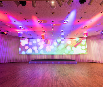 Der größte Veranstaltungsaal im Haus der Bayerischen WIrtschaft, der Europasaal ist mit stimmungsvollen rosa Licht ausgeleuchtet. Auf der großen Panoramaleinwand sind bunte Lichtpunkte und Reflexe zu sehen.