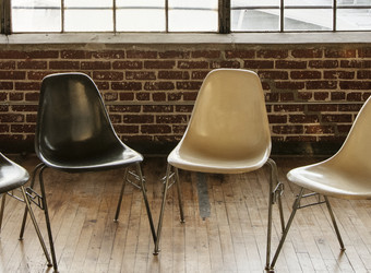 Foto von schwarzen und beigen Stühlen aus Kunststoff mit Metallbeinen, die in einem Halbkreis in einem Raum mit Backsteinwänden und Industriefenstern Kassettenfenster stehen. Der Fußboden ist helles Parkett Holzfußboden.